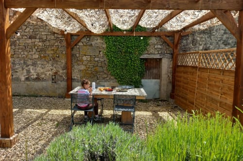 Terrasse couverte de pergola à La Maison De Fleurat à Domeyrot avec table de repas et murs en pierre couverts de lierre