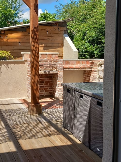 Terrasse extérieure de La Maison De Fleurat avec cheminée en briques, pergola en bois et vue sur les jardins de Domeyrot