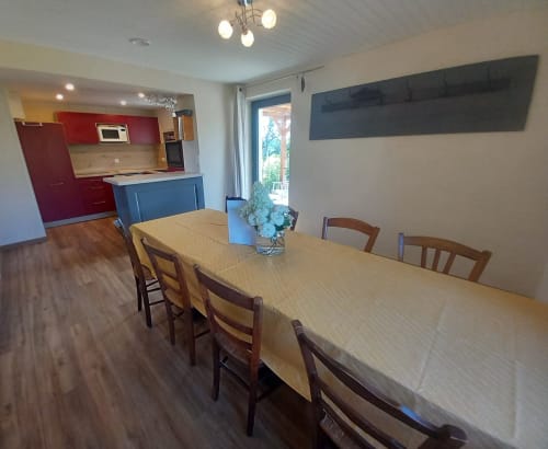 Salle à manger avec table et chaises en bois, cuisine moderne aux armoires rouges, îlot bleu à La Maison De Fleurat