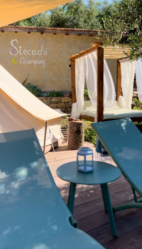 Jardin lounge Stecadò Glamping avec chaises bleues, gazebo aux rideaux blancs et oliviers à Dolceacqua
