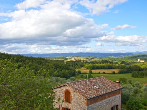 Villa in pietra con tetto in cotto che affaccia sul castello di Monteriggioni e il paesaggio collinare toscano con verdi colline