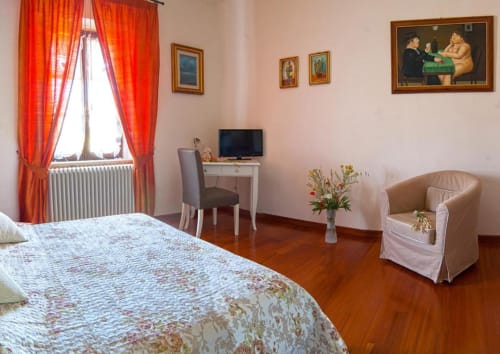 Ampia camera da letto presso B&B Torre Della Chiocciola con letto, poltrona, scrivania con TV e vivaci tende rosse a Monteriggioni