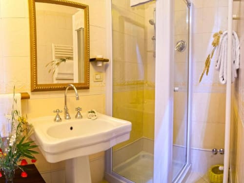 Bagno luminoso con lavabo su colonna bianca, specchio con cornice dorata e doccia walk-in presso B&B Torre Della Chiocciola
