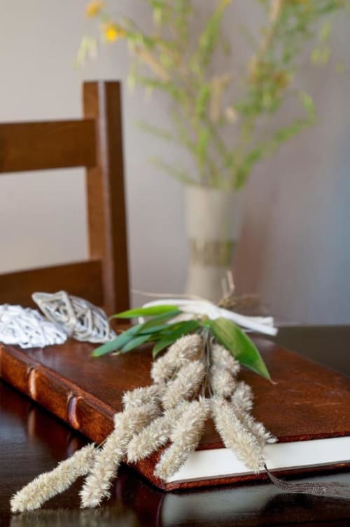 Scrivania di B&B toscano con libro aperto, erbe secche e fiori freschi a Monteriggioni