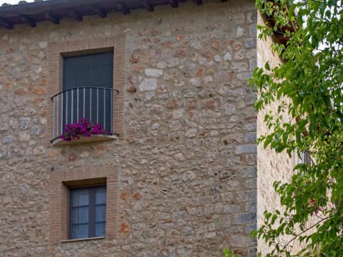 Facciata in pietra della Torre Della Chiocciola B&B a Monteriggioni con edera e fiori viola al balcone