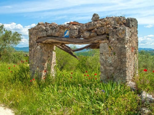 Rovine di un arco in pietra con trave di legno in un prato di fiori selvatici vicino a Monteriggioni, Siena