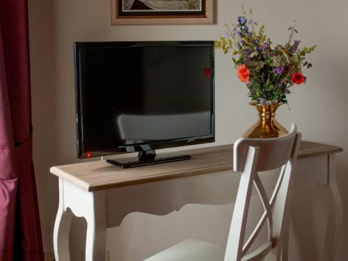 Elegante scrivania di hotel con TV a schermo piatto, sedia bianca e fiori freschi in vaso di ottone a Torre Della Chiocciola