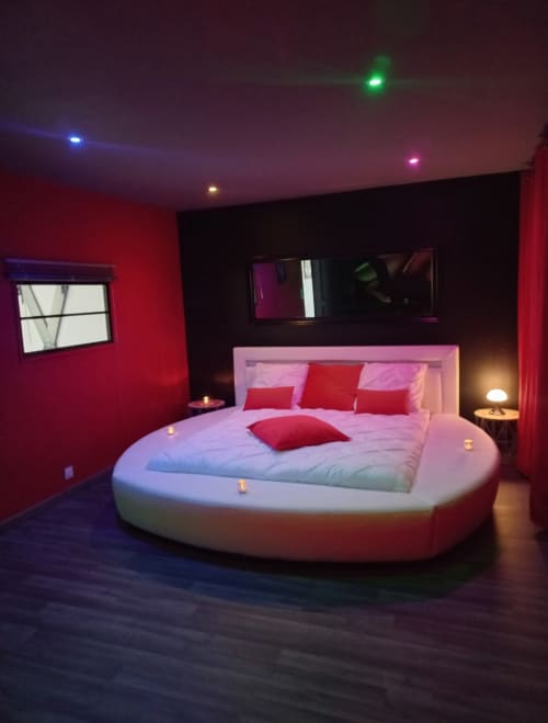 Chambre de villa de luxe avec lit rond, accents rouges et éclairage ambiant à La Maison du Plaisir