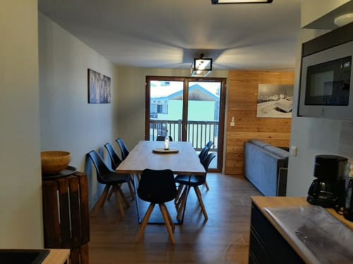 Vue depuis la cuisine de l'appartement 204B dans la résidence l'Albane à Vars-les-Claux, montrant une grande table à manger pour 12 personnes, parfaite pour des repas conviviaux en famille ou entre amis dans un cadre chaleureux.