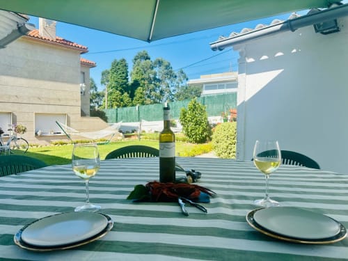 Mesa de comedor al aire libre con vino y mariscos bajo toldo verde en la casa rural Casa Caeiro en Baiona, España