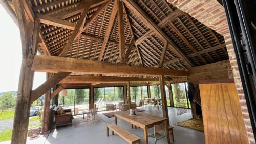 Intérieur rustique de la grange du Domaine de Blanvatel avec poutres en bois, table de salle à manger et vues sur la campagne