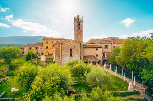 Torre medievale e edifici in pietra circondati dal verde lussureggiante a Monteriggioni, Siena, Italia