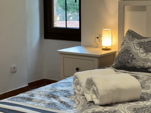 Chambre accueillante de l'auberge Can Ricós à Vallgorguina avec serviettes roulées, coussins motifs, lampe de chevet et vue sur la fenêtre.