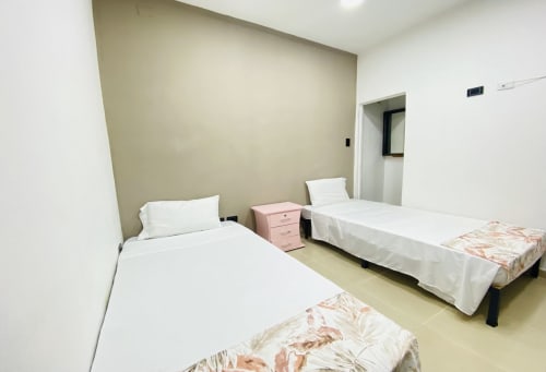 Habitación doble en hotel Casa Mango de Cali con ropa de cama blanca, mesita de noche rosa y pared de acento beige