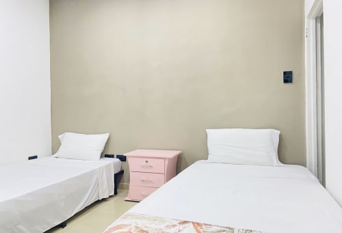 Dos camas individuales con sábanas blancas y mesita de noche rosa en habitación luminosa del hotel CASA MANGO en Cali, Colombia