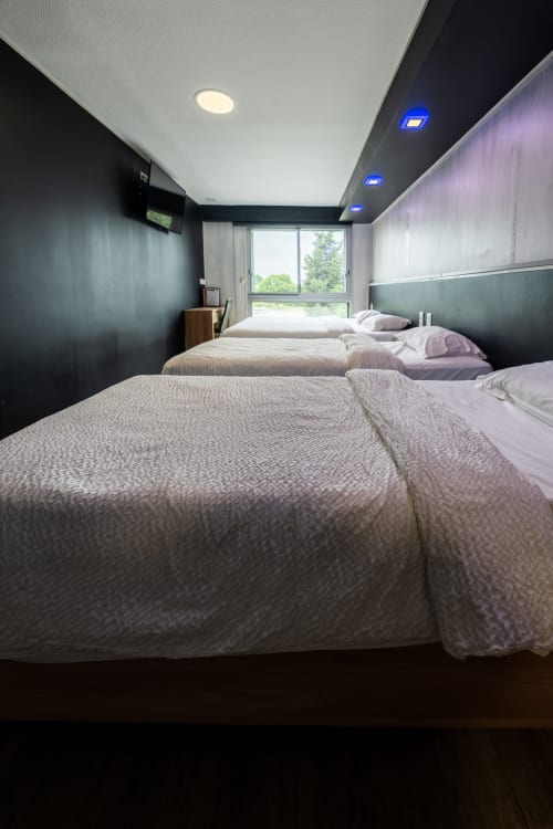 Espaciosa habitació familiar a l'Hôtel Rocade de Pamiers amb tres llits, vista al jardí, il·luminació moderna i paret d'accent fosca