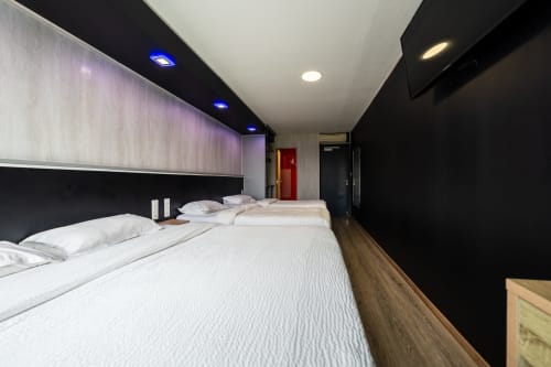 Habitació familiar moderna a l'Hôtel Rocade Pamiers amb dos llits, paret accent negra, llums LED blaus i sòl de fusta
