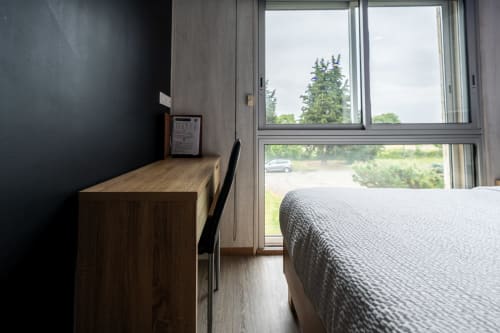 Habitació moderna de l'Hôtel Rocade a Pamiers amb llit, escriptori i vista al jardí a través de portes corredisses de vidre