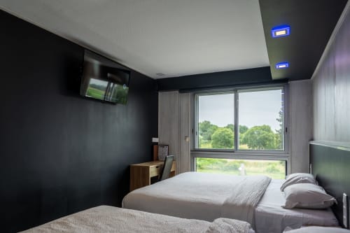 Habitació familiar moderna a l'Hôtel Rocade de Pamiers amb dos llits, vista al jardí per grans finestres, TV, escriptori i disseny contemporani