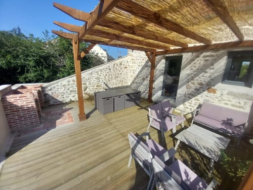 Terrasse en bois de la villa La Maison De Fleurat avec chaises longues, pergola et vue sur le bâtiment en pierre à Domeyrot
