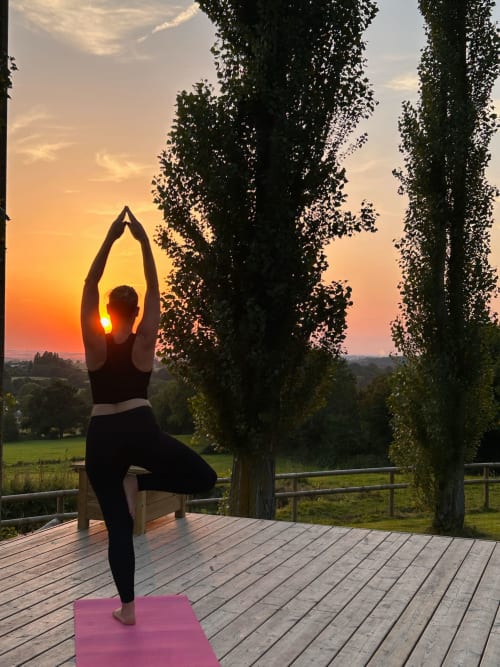 Woman in yoga pose at sunset on wooden deck overlooking Normandy countryside at Domaine de Blanvatel