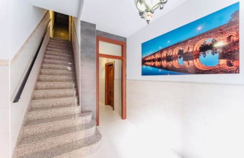 Pasillo moderno en apartamento de Mérida con escaleras, puerta roja y obra de arte arquitectónica azul en paredes blancas