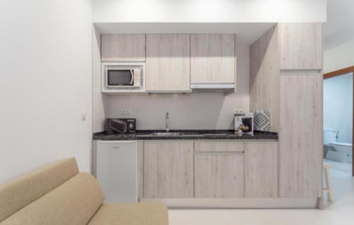 Cocina moderna con muebles de madera clara, encimera negra y electrodomésticos en apartamento Gestyp-AT, Mérida