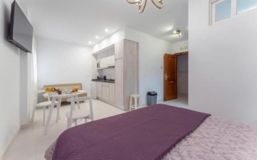 Moderno apartamento estudio en Mérida con cama de sábanas moradas, cocina blanca, comedor y vistas a la ciudad