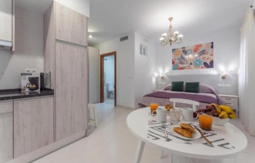 Moderno apartamento estudio en Mérida con cocina, comedor y cama, decorado con arte colorido e iluminación de lámparas colgantes