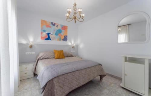 Dormitorio moderno en apartamento Gestyp-AT en Mérida con cama gris, araña dorada, cuadros coloridos y espejo redondo
