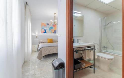 Baño y dormitorio moderno del hotel en Mérida con ducha, lavabo y cama con almohada decorativa amarilla
