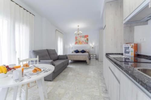 Moderno apartamento estudio en Mérida con cocina abierta, sala de estar, sofá gris y dormitorio con vistas a la ciudad