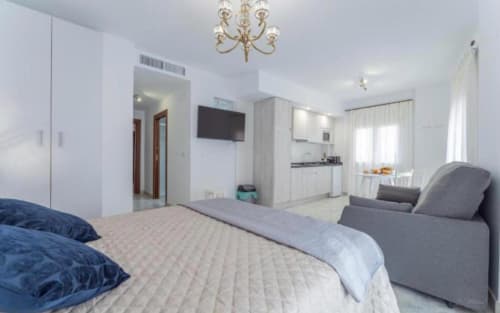 Moderno apartamento estudio en Mérida con cama, cocina americana, sofá, TV y vistas a la ciudad desde ventanas luminosas