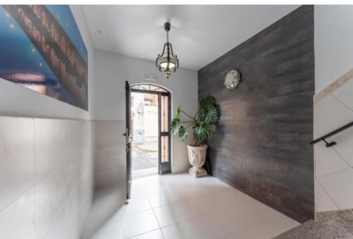 Elegante recibidor de apartamento moderno en Mérida con pared de acento oscuro, pisos de azulejo blanco, planta en maceta y lámpara colgante decorativa.