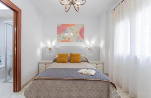 Dormitorio luminoso del apartamento Gestyp-AT en Mérida con cabecero gris, almohadas amarillas y obra floral