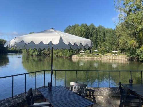 Terrasse de restaurant en bord de rivière au Moulin De La Chevrière avec parasol blanc festonné surplombant la rivière Saché
