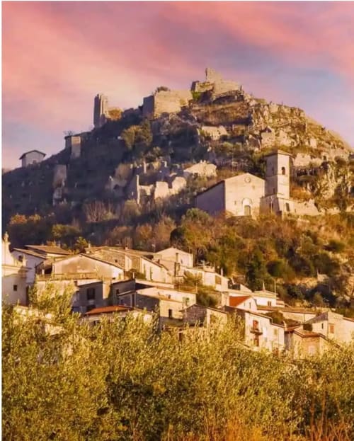 Ruderi di castello medievale e edifici bianchi su collina a Roccasecca, Italia al tramonto con ulivi