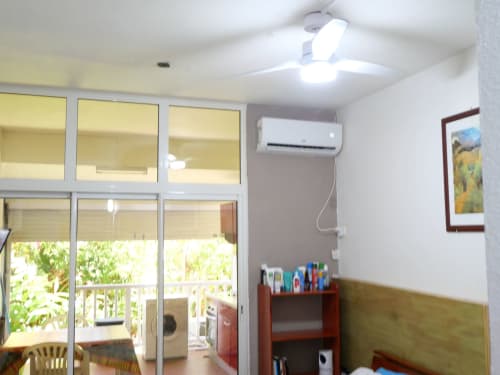 Studio apartment interior with ceiling fan, air conditioning unit, and glass doors overlooking garden at Studio Face Marina,