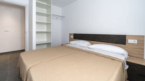Dormitorio moderno en Apartamentos Burriana con camas gemelas, cabecero de madera, estanterías blancas y ropa de cama beige