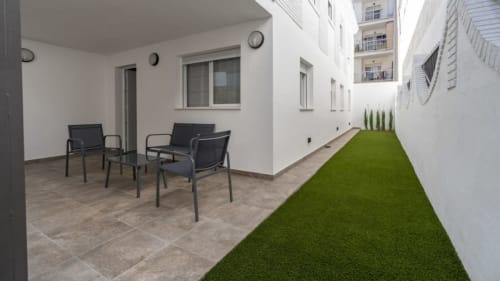 Patio moderno de Apartamentos Burriana con zona de estar, césped artificial y muros blancos en España