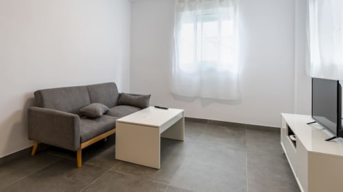 Sala de estar moderna en Apartamentos Burriana con sofá gris, mesa de centro blanca y zona de televisión