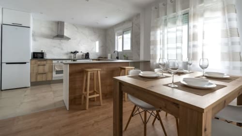 Cocina y comedor moderno en Apartamentos Burriana con encimeras de madera, electrodomésticos blancos y mesa servida