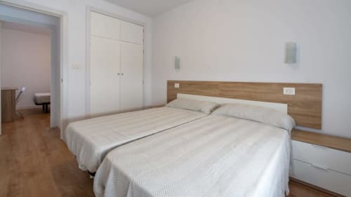 Dormitorio espacioso en Apartamentos Burriana con cama doble, cabecero de madera, armario y suelo de madera