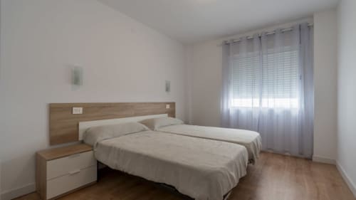 Dormitorio moderno en Apartamentos Burriana con camas gemelas, cabecero de madera y luz natural de amplio ventanal