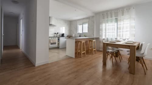 Cocina abierta moderna y zona de comedor en Apartamentos Burriana con suelos de madera, muebles blancos y barra de desayuno