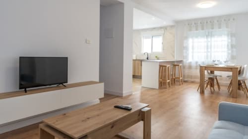 Sala de estar moderna en Burriana con TV, muebles de madera, cocina abierta y comedor integrado