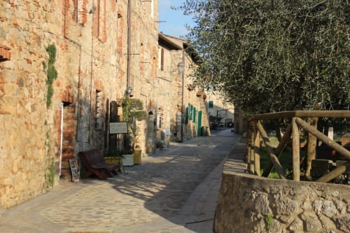 Affascinante vicolo in pietra a Monteriggioni con edifici rustici e ulivi presso Torre Della Chiocciola B&B
