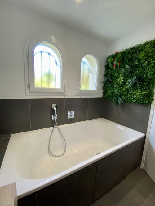 Salle de bain spa moderne aux chambres Lady Jule avec baignoire îlot blanche, baies vitrées cintrées, murs en carrelage noir et mur végétal vivant