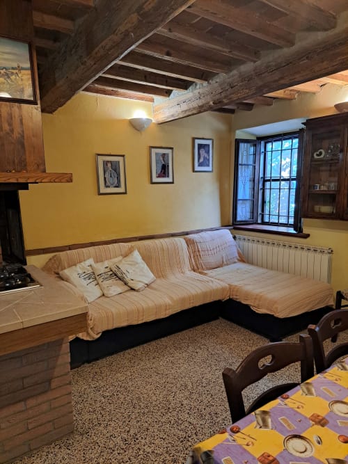 Soggiorno rustico nella villa Corte Pincione a Montecarlo con travi in legno a vista, divano rigato, pareti gialle e quadri incorniciati