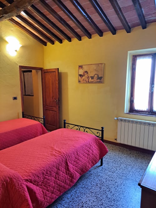 Camera da letto giallo brillante alla villa Corte Pincione a Montecarlo con letti gemelli, travi in legno scuro e arredamento d'epoca